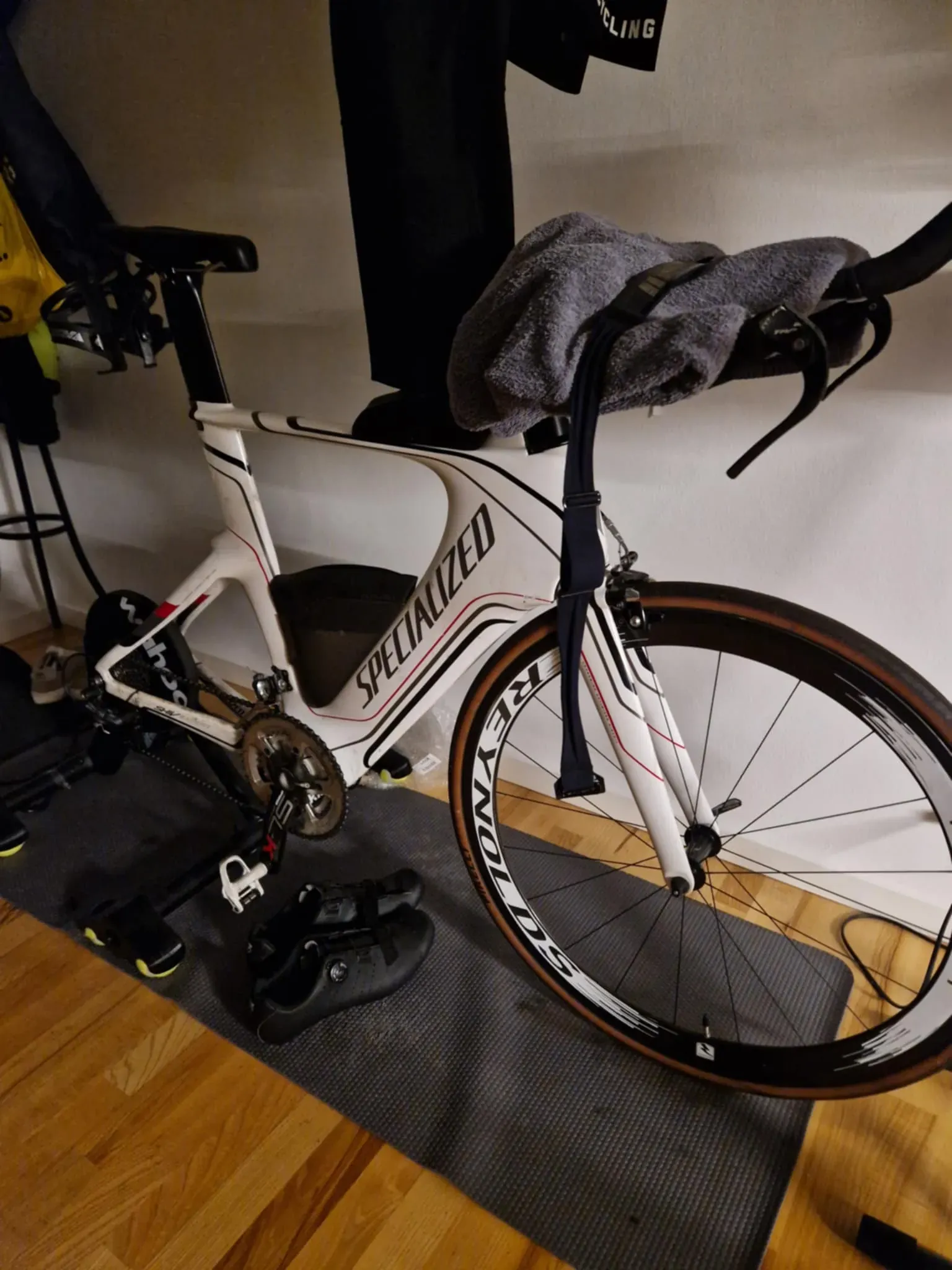 A white Specialized time trial bike on a direct-drive trainer, with a grey towel folded over the aerobars and shoes on the mat